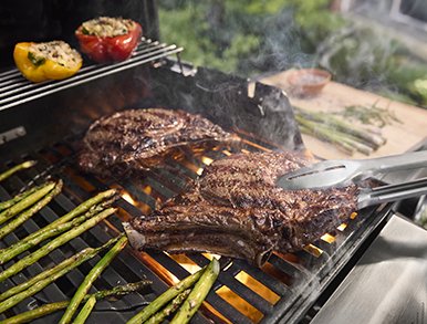 Tomahawk steak and asparagus grilling with flames