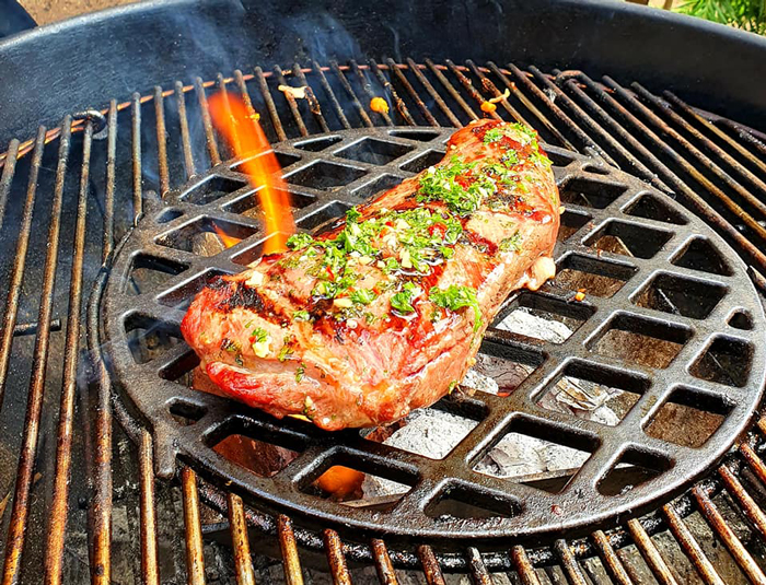 Herb-crusted steak searing on a Weber grill grate