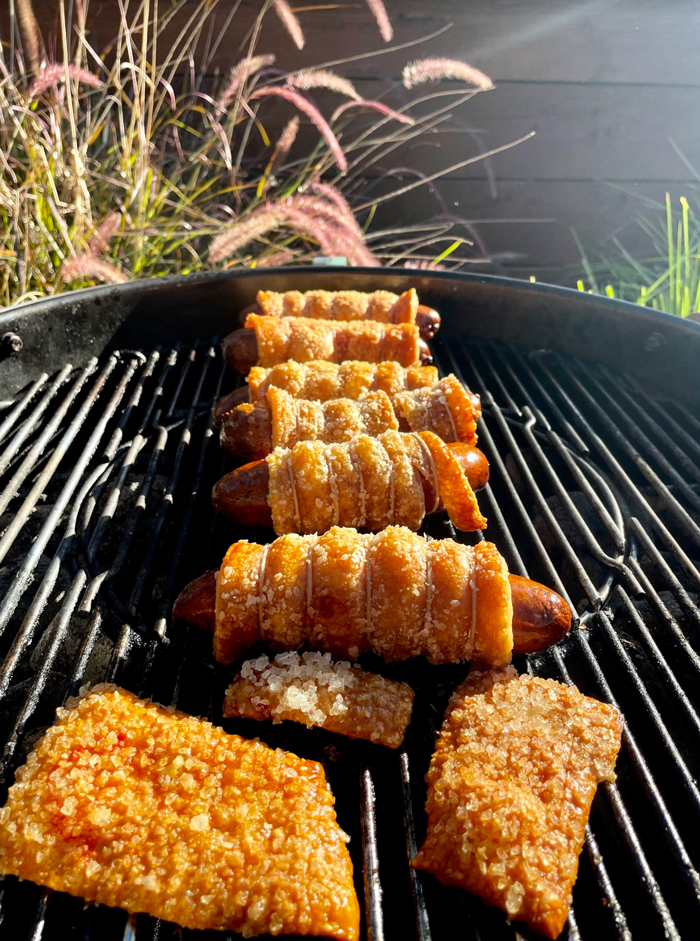 Bacon-wrapped sausages and crackling cooking on a Weber grill