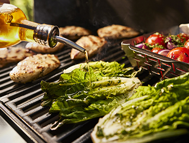 Olive oil being poured over grilled cos lettuce and vegetables