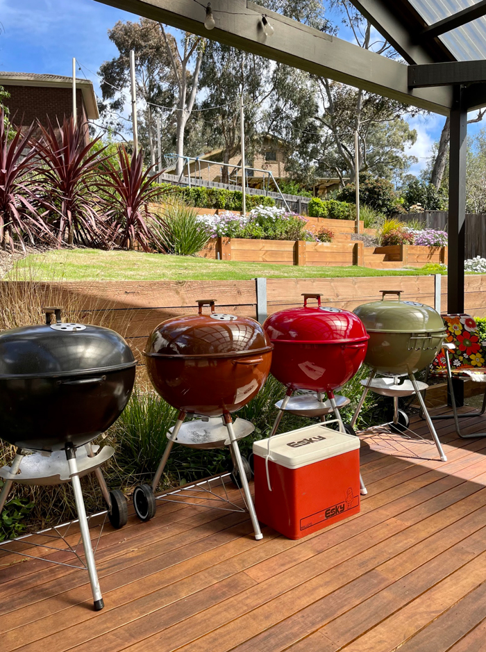 Row of black, copper, red and olive Weber kettles on a timber deck