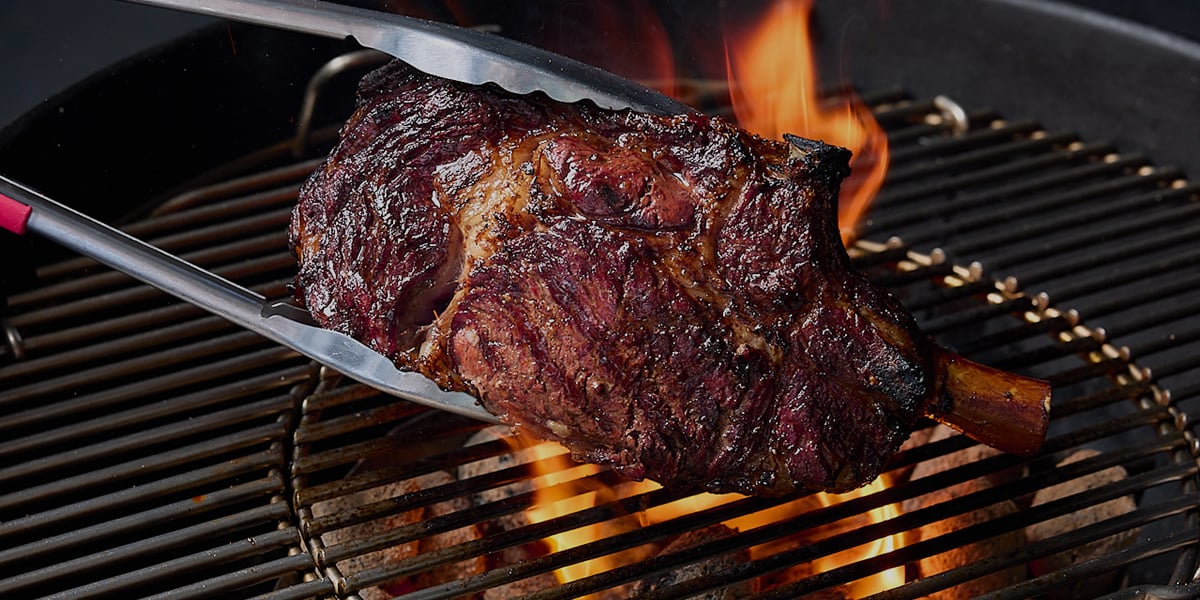 A flame-grilled tomahawk steak cooking on a Weber barbecue