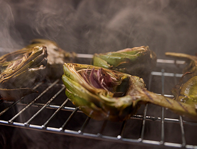 Halved artichokes smoking on the grill