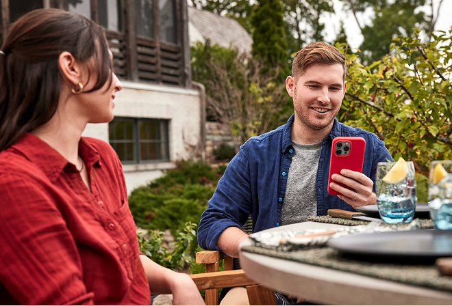 Couple relaxing at an outdoor table while a man checks BBQ doneness on the Weber Connect app on his mobile phone.