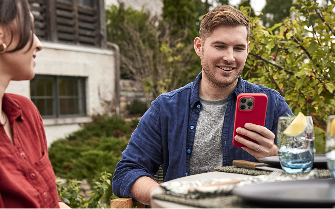 Ein Paar sitzt drau&szlig;en an einem Tisch, eine Person schaut auf ein Smartphone