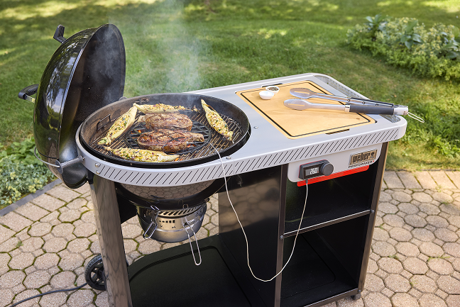 Weber Performer Smart Holzkohlegrill, auf dem Fleisch gegrillt wird, das zur &Uuml;berwachung der Temperatur &uuml;ber die Weber Connect App angeschlossen ist.