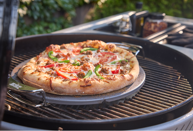 Weber Performer charcoal barbecue with Weber Crafted grillware&mdash;such as sear grate or pizza stone&mdash;showing versatile cooking options.