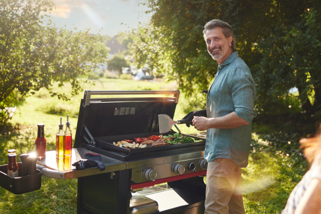 Ein Mann grillt zufrieden im Freien auf einer Weber Slate Plancha.