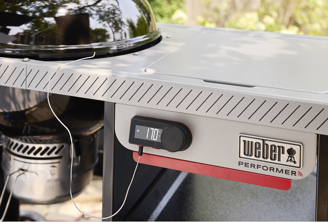 Weber Performer charcoal barbecue paired with the Weber Connect app on a smartphone, displaying real‑time cooking guidance.