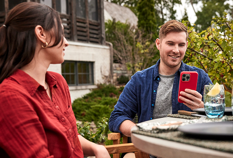 Et par som slapper av ved et bord og venter med Weber Connect-appen p&aring; en mobiltelefon