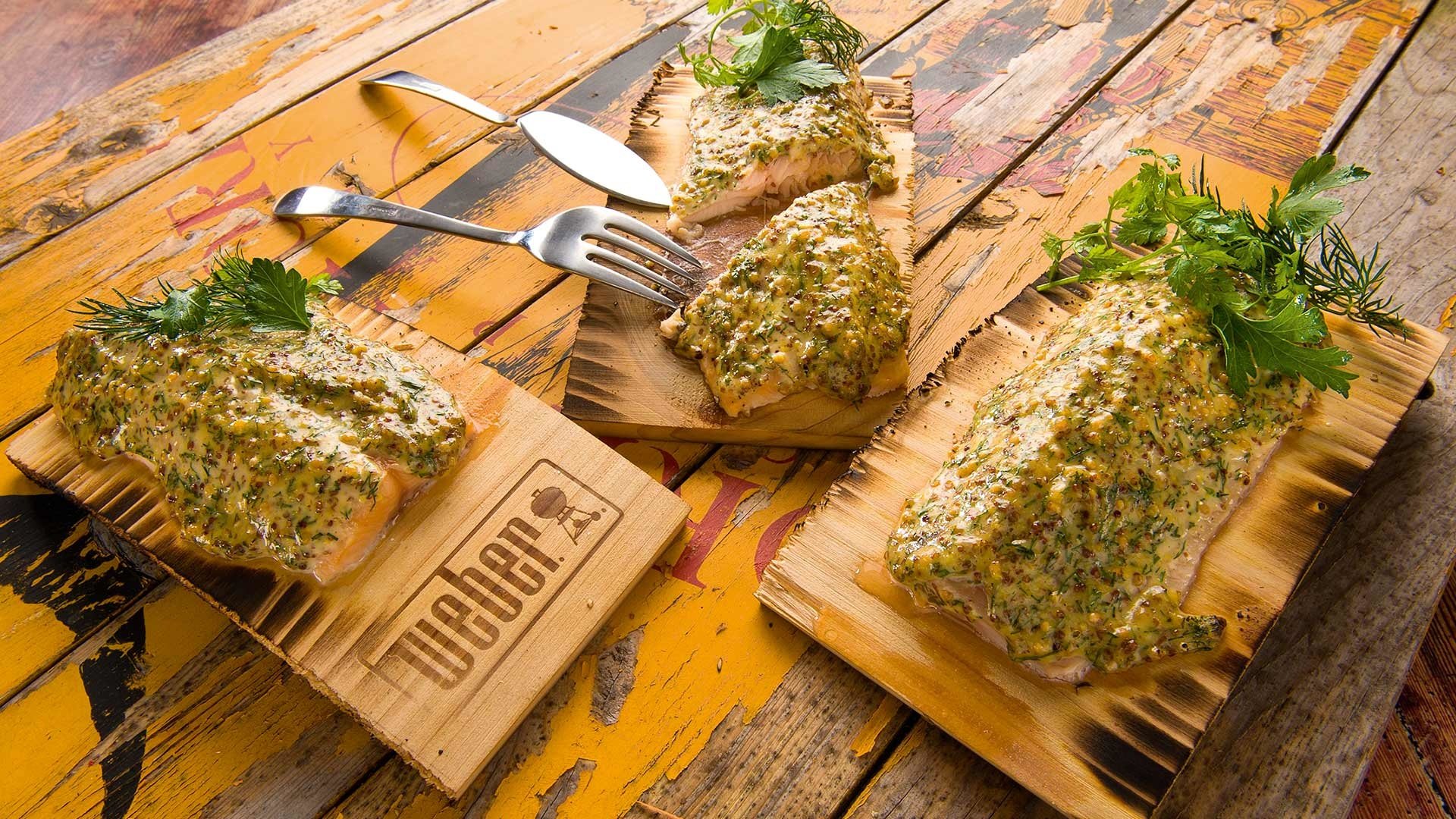  Saiblingsfilet unter Dill-Senfglasur auf dem Zedernholzbrett gegrillt, garniert mit frischen Kräutern


