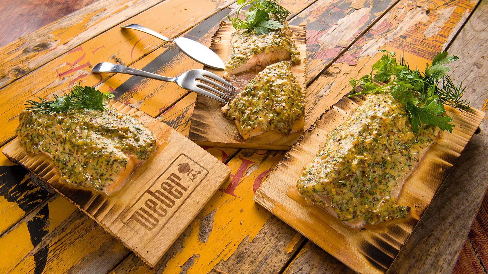  Saiblingsfilet unter Dill-Senfglasur auf dem Zedernholzbrett gegrillt, garniert mit frischen Kräutern



